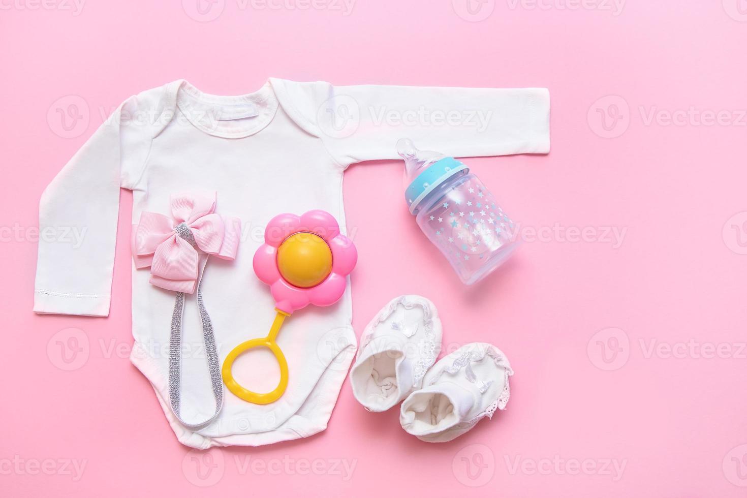 bodysuit, rattle, booties, bottle, pink bow for a newborn on a pink background photo