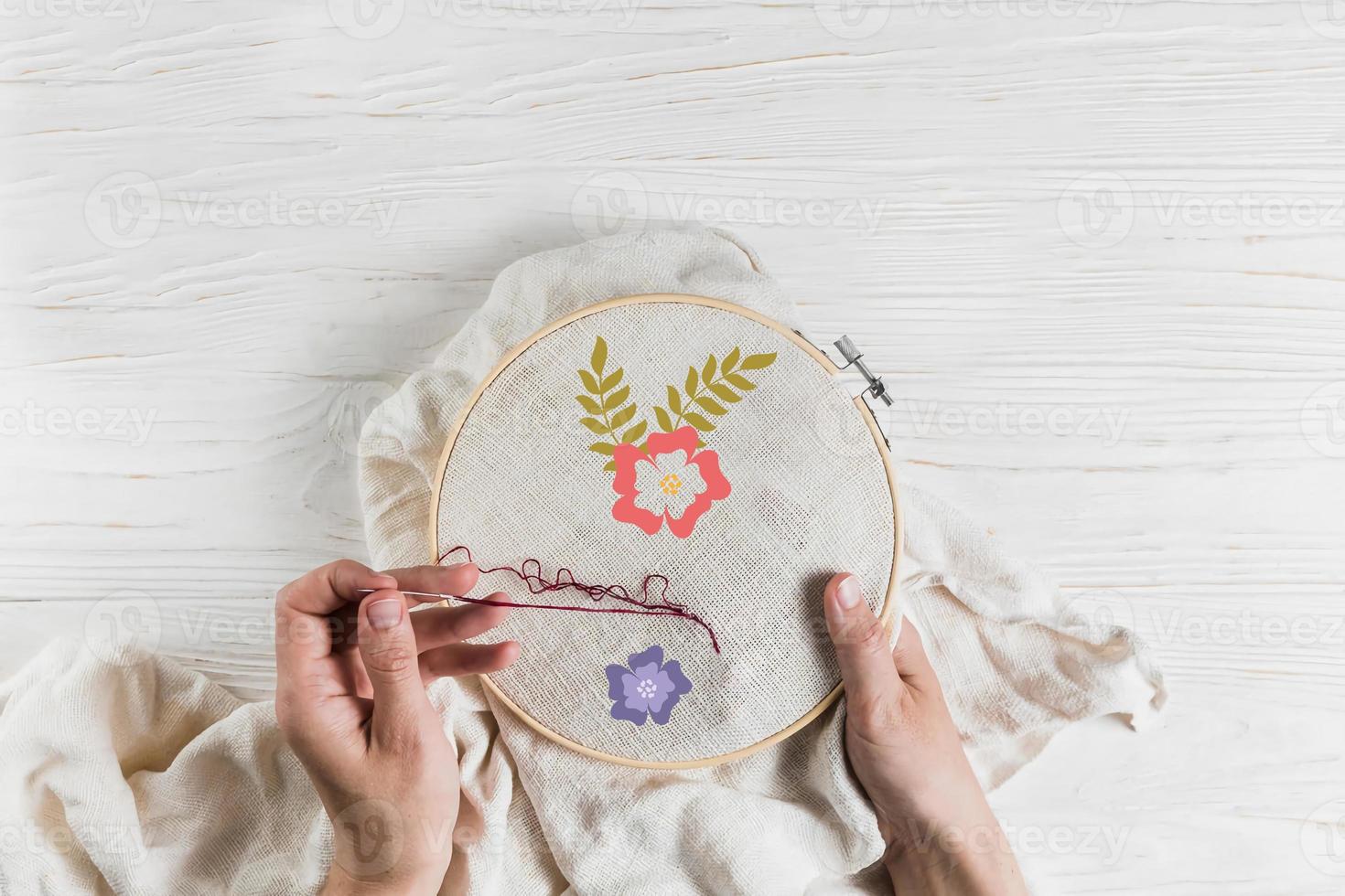 Woman doing handicraft embroidery work on white wooden background. photo