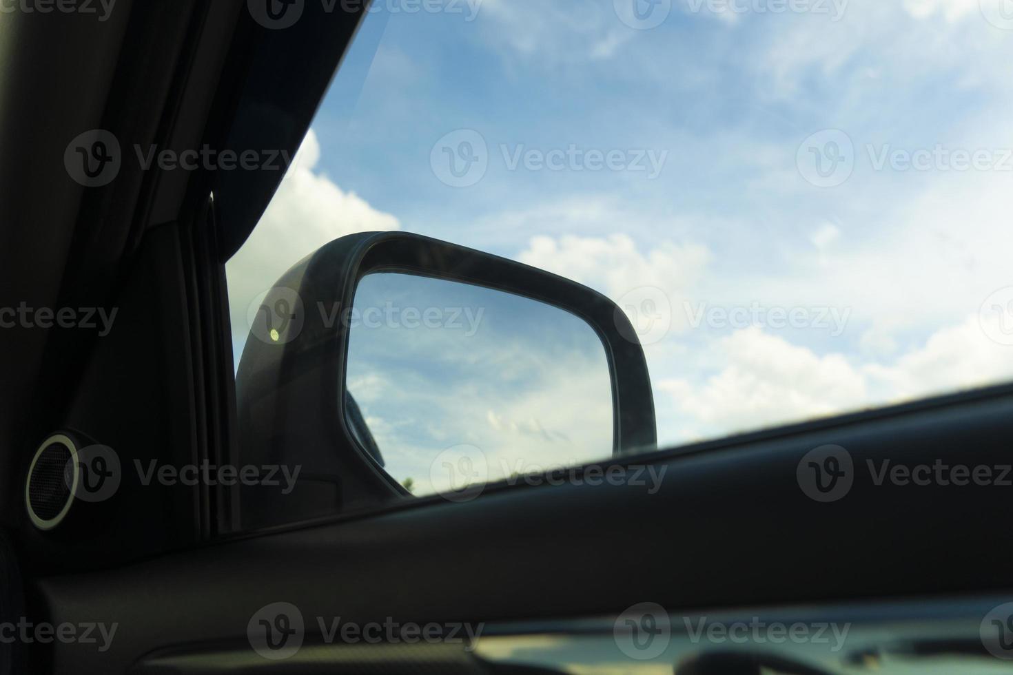 View of inside car focus on mirror side of car. View to the blue sky and white clouds. photo