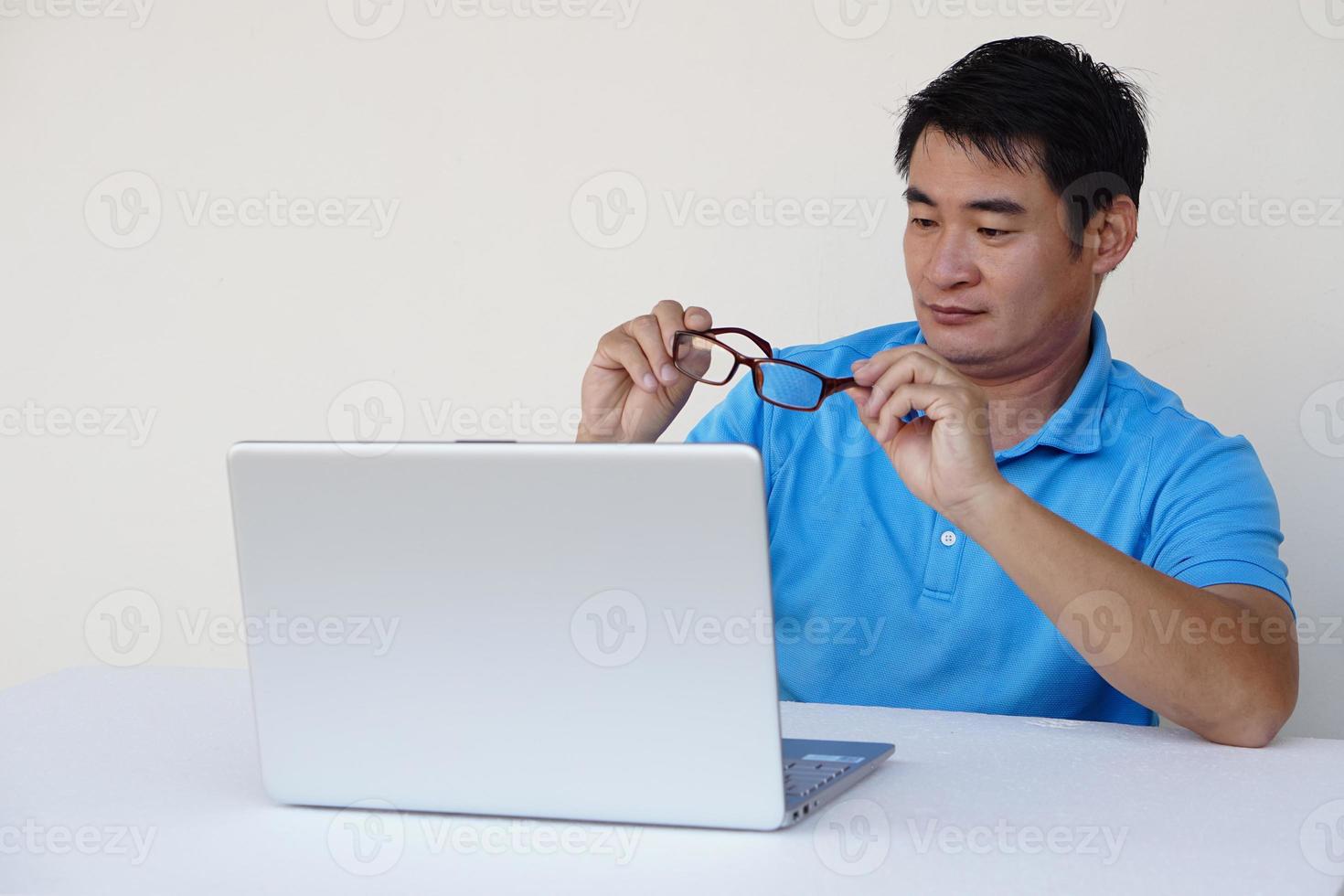 el hombre asiático sostiene anteojos durante el trabajo en la computadora portátil. concepto, problema de la vista. optometría. anteojos con lentes convexas o cóncavas. miopía.enfermedad ocular foto