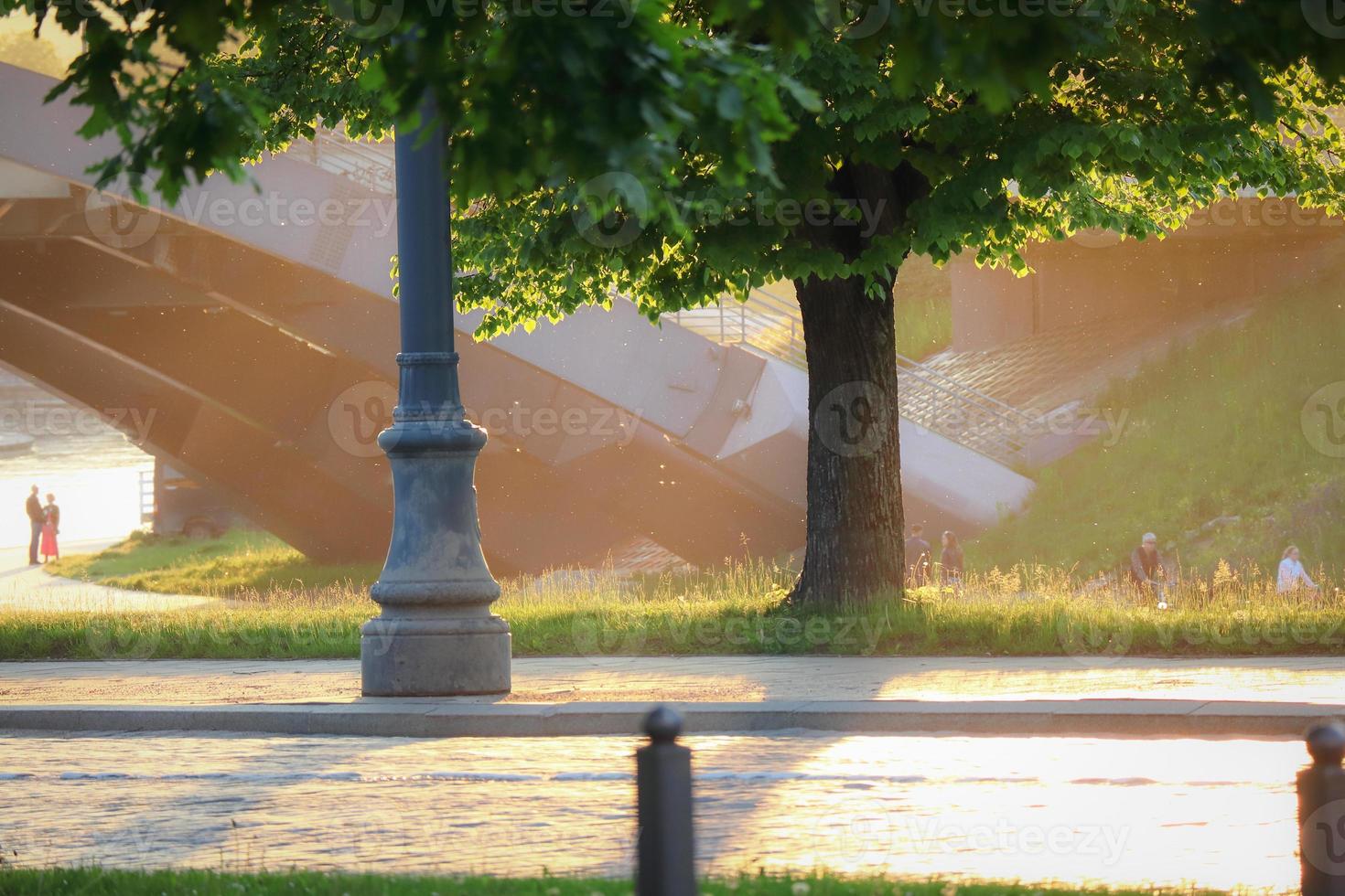 orilla del río vilnius con puente a la luz del sol atmósfera mágica cruce de carreteras con árbol y luz de la calle y gente borrosa en el fondo foto