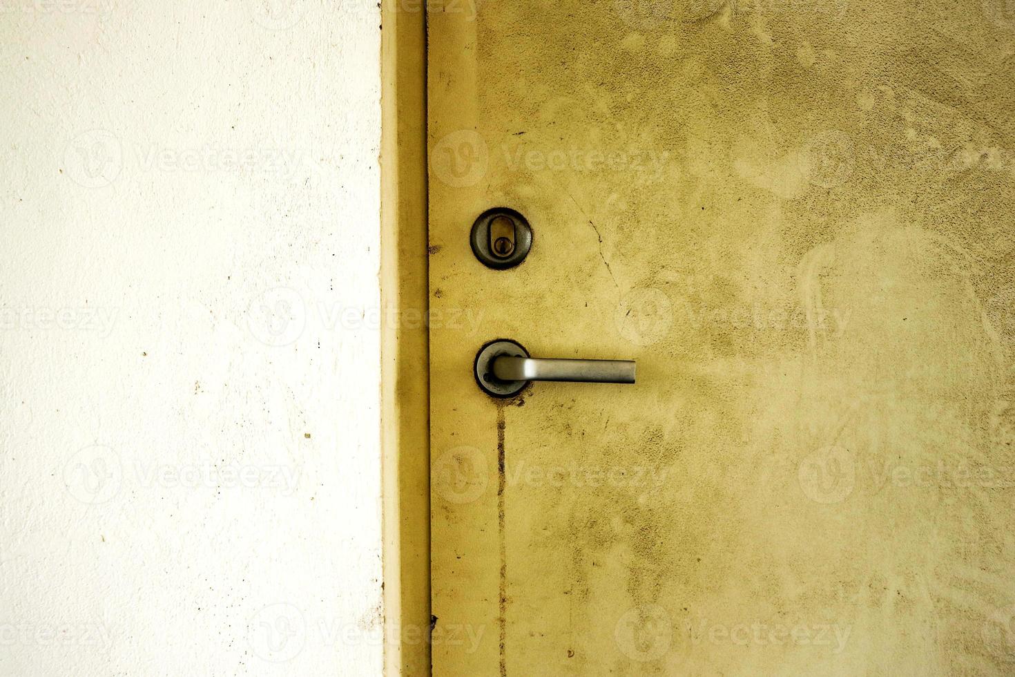 Yellow old weathered dirty door in light concrete wall with a metal handle and a keyhole photo