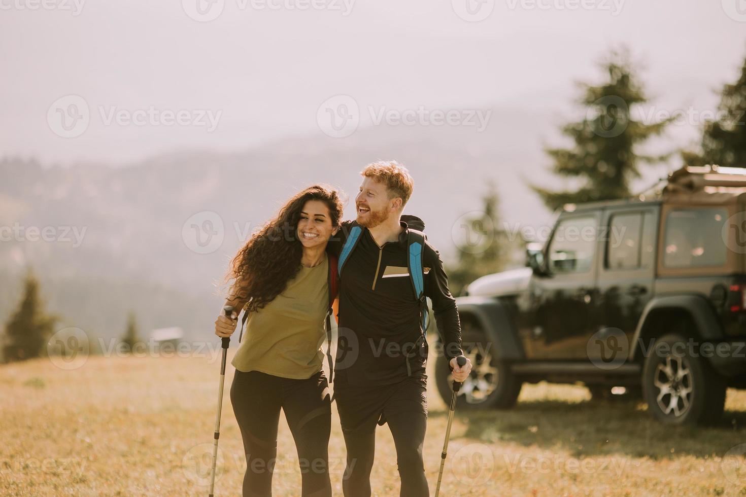 Smiling couple starting walking with backpacks over green hills photo