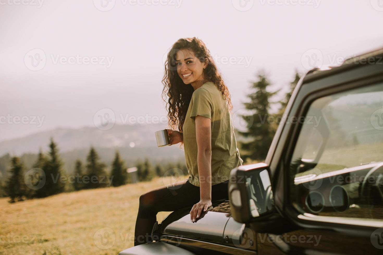 mujer joven relajándose en el capó de un vehículo de terreno en el campo foto