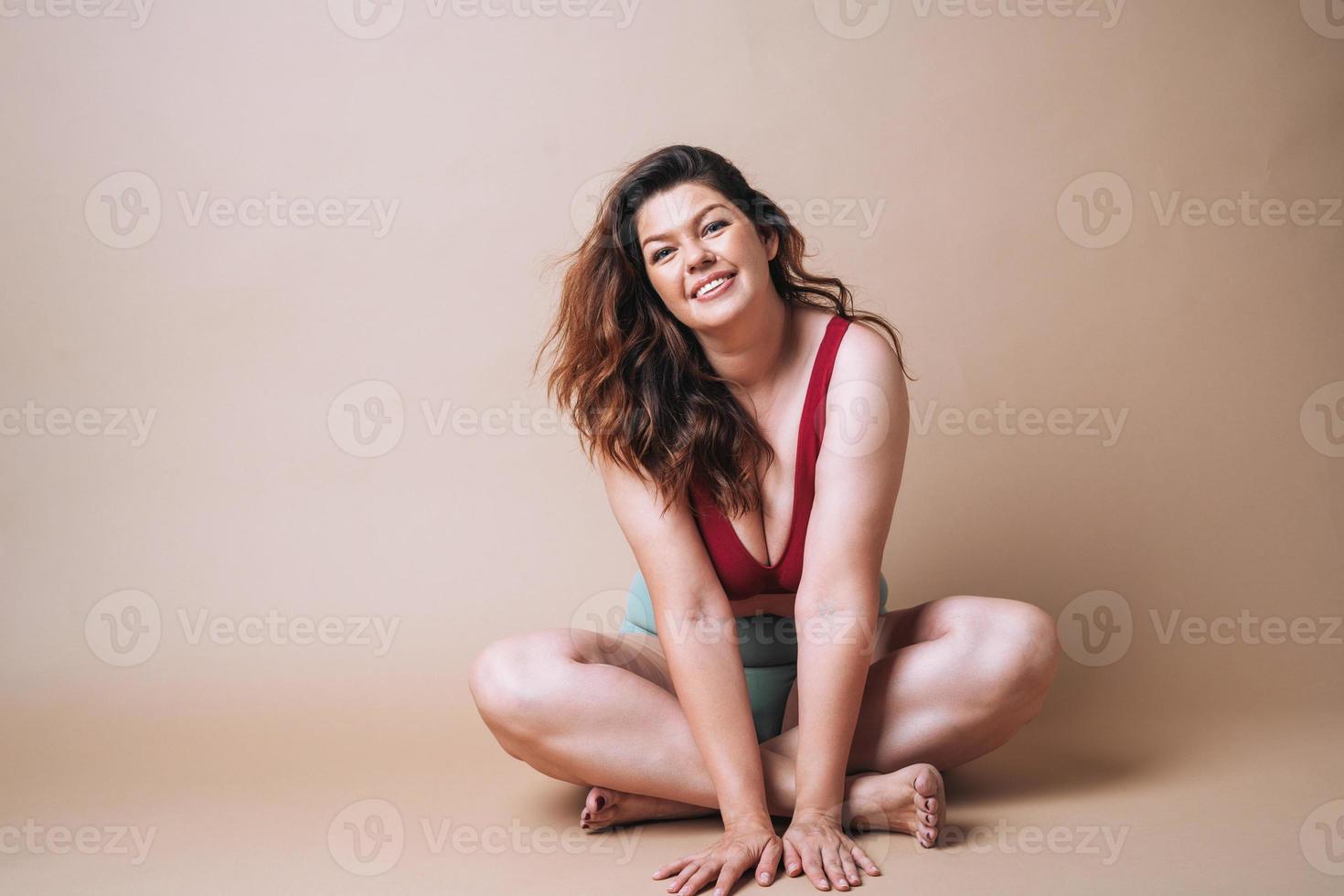 mujer joven amante de sí misma de talla grande en ropa interior sentada en un fondo beige, amor corporal foto