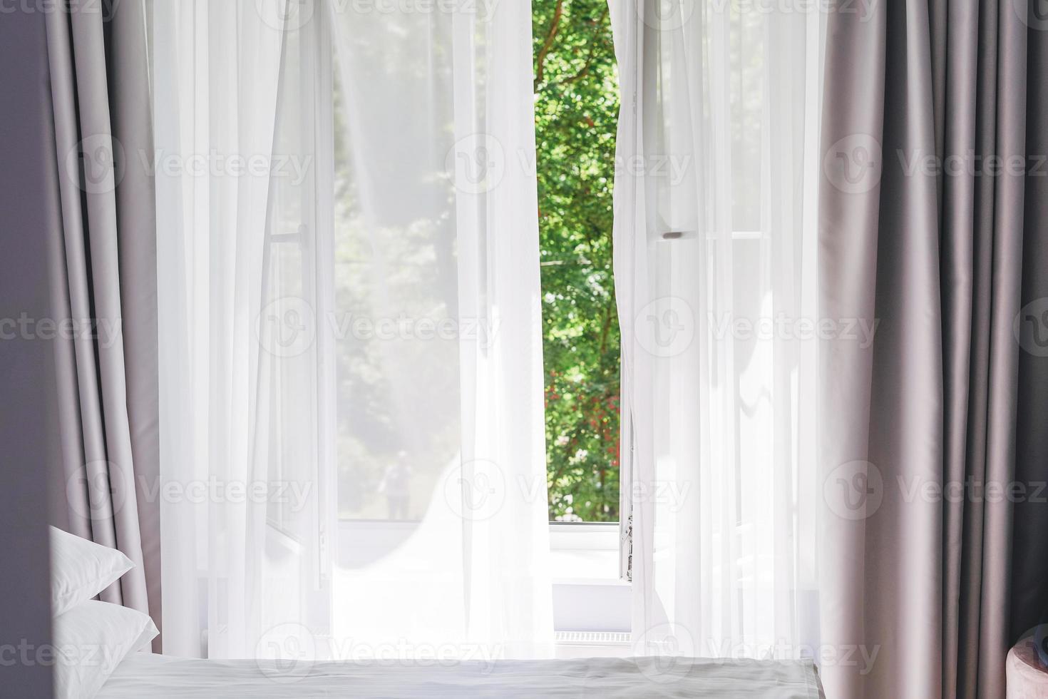 White tulle curtains on the window with green trees on background at home photo