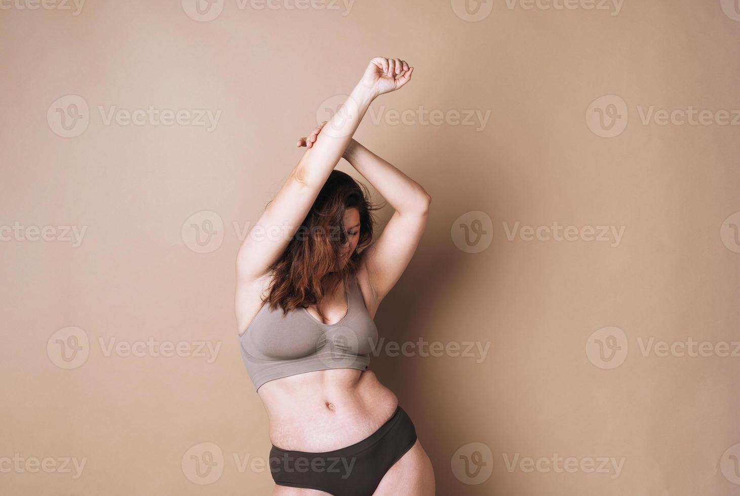 joven atractiva mujer de talla grande en ropa interior bailando sobre fondo beige, amor corporal foto