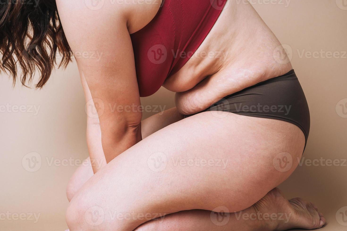 Crop photo of real young woman plus size in underwear sitting on beige background, body love