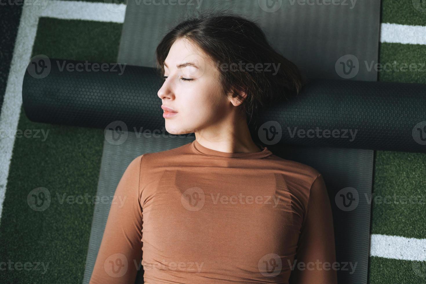 Young brunette woman doing stretching pilates on massage roll in the fitness club gym photo