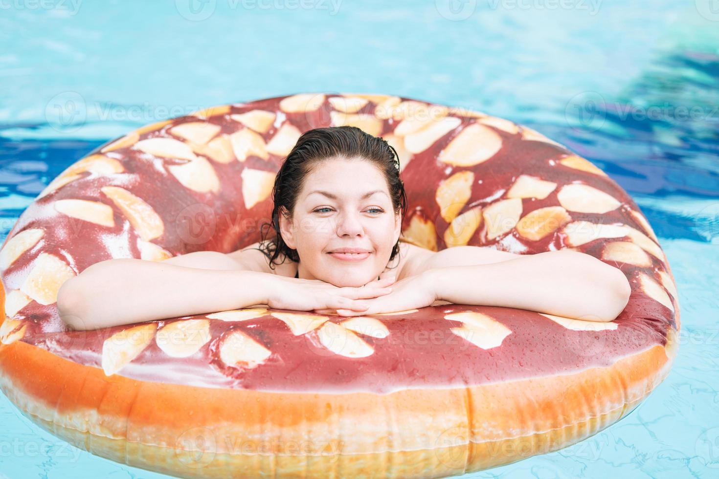 Happy young woman plus size body positive in inflatable doughnut circle swimming in the pool, summer vacations photo