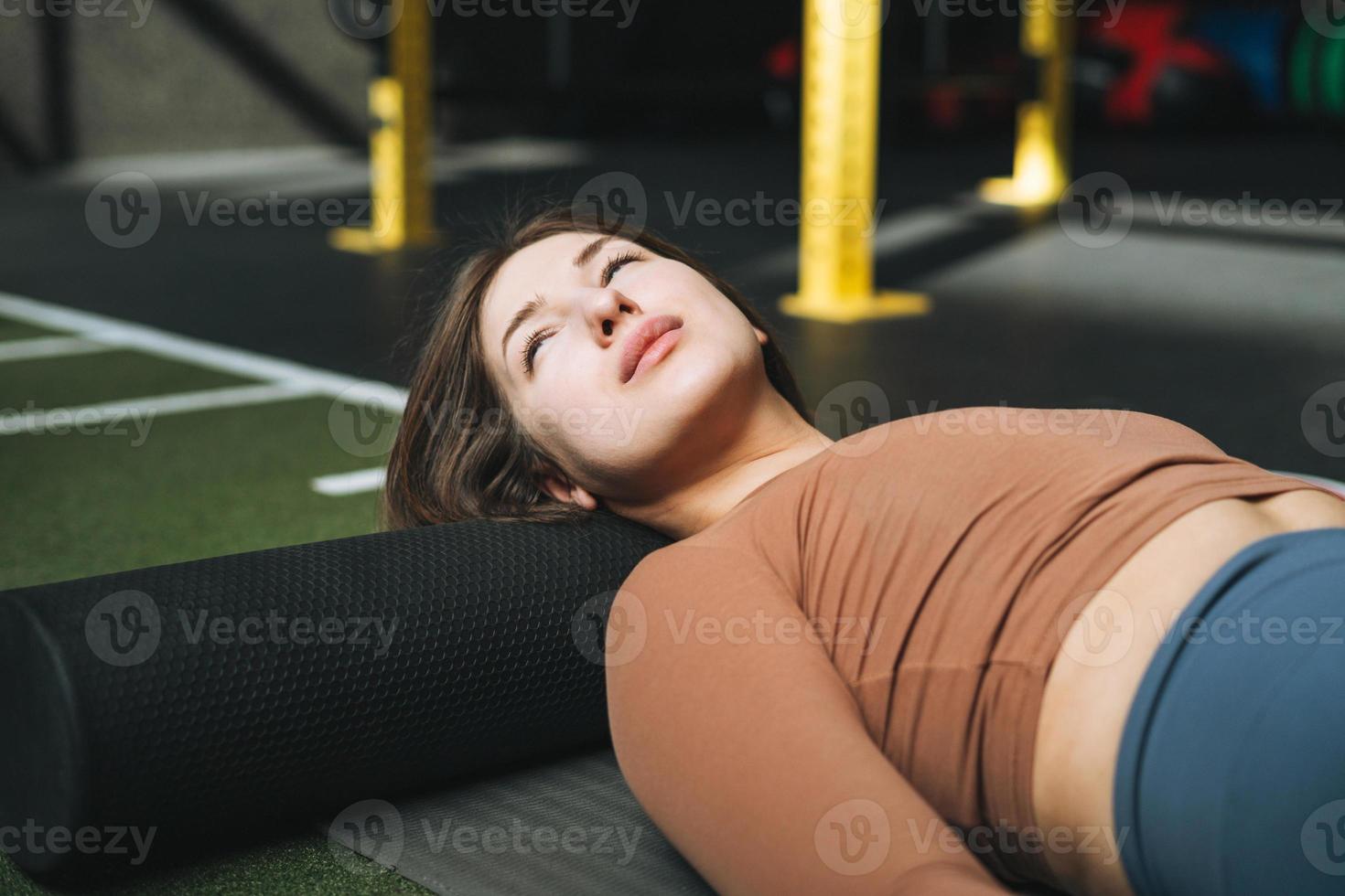 Young brunette woman doing stretching pilates on massage roll in fitness club gym photo