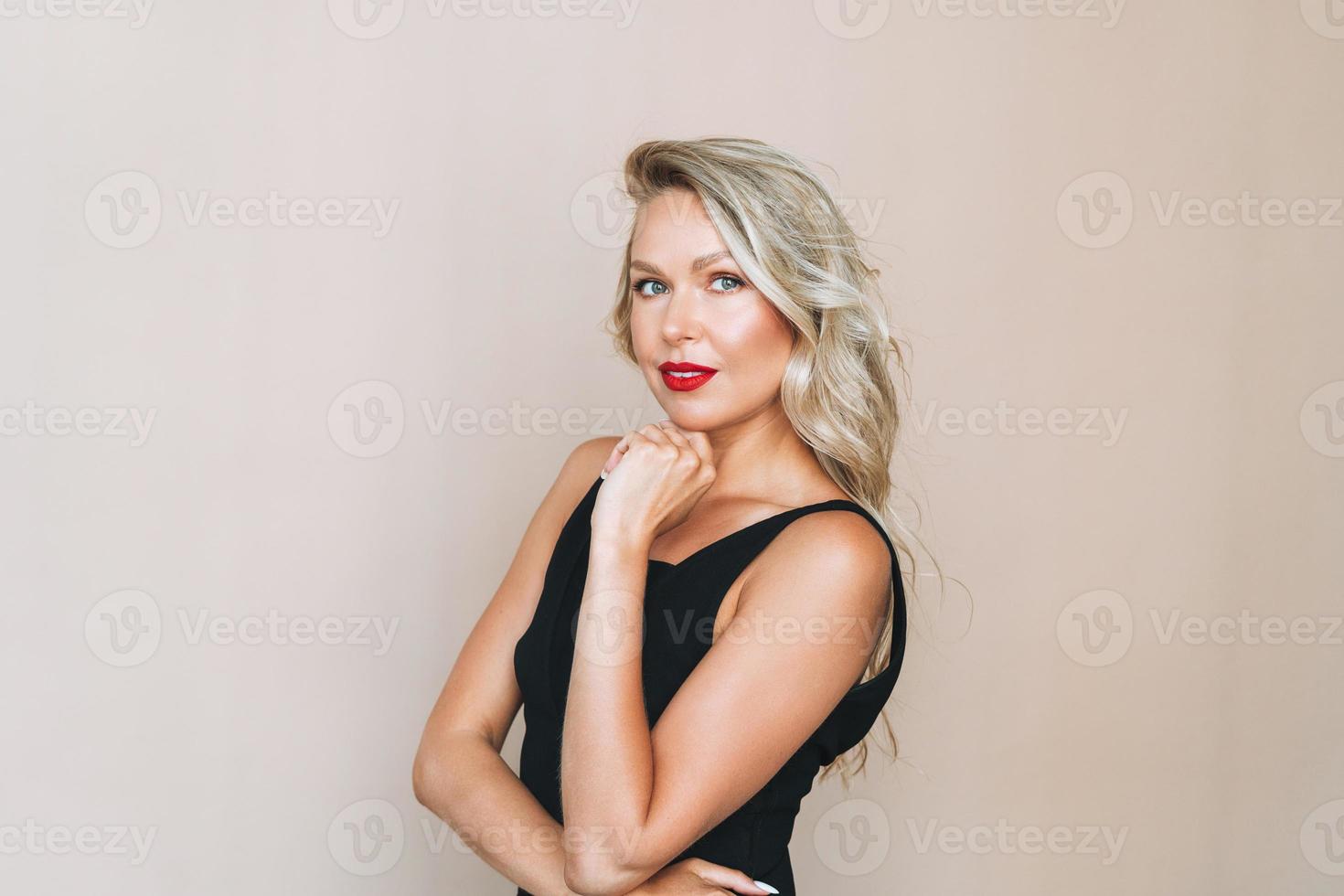 Portrait of gorgeous happy blonde young woman with bright makeup in evening dress on beige background photo