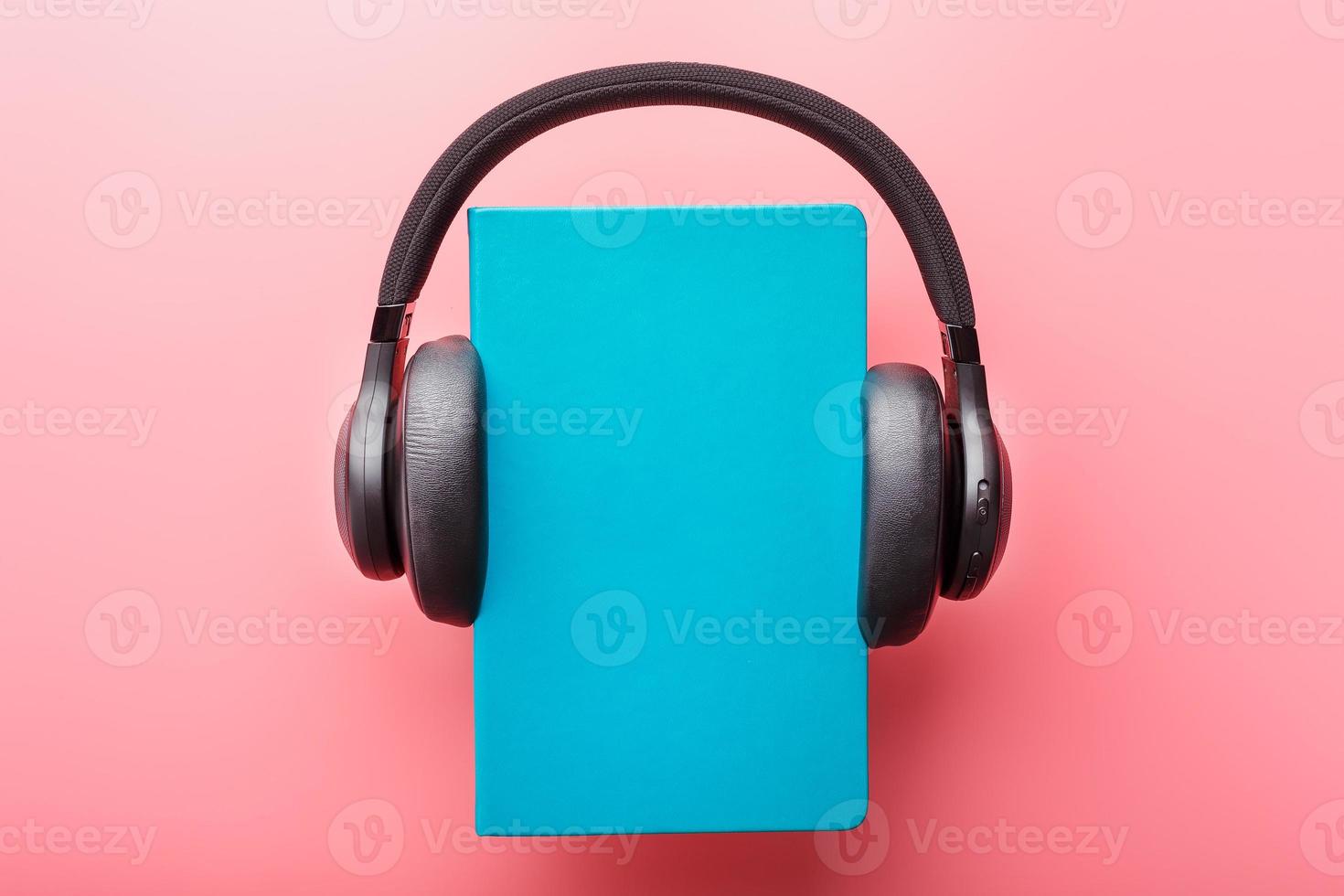 Headphones are worn on a book in a blue hardcover on a pink background, top view. photo