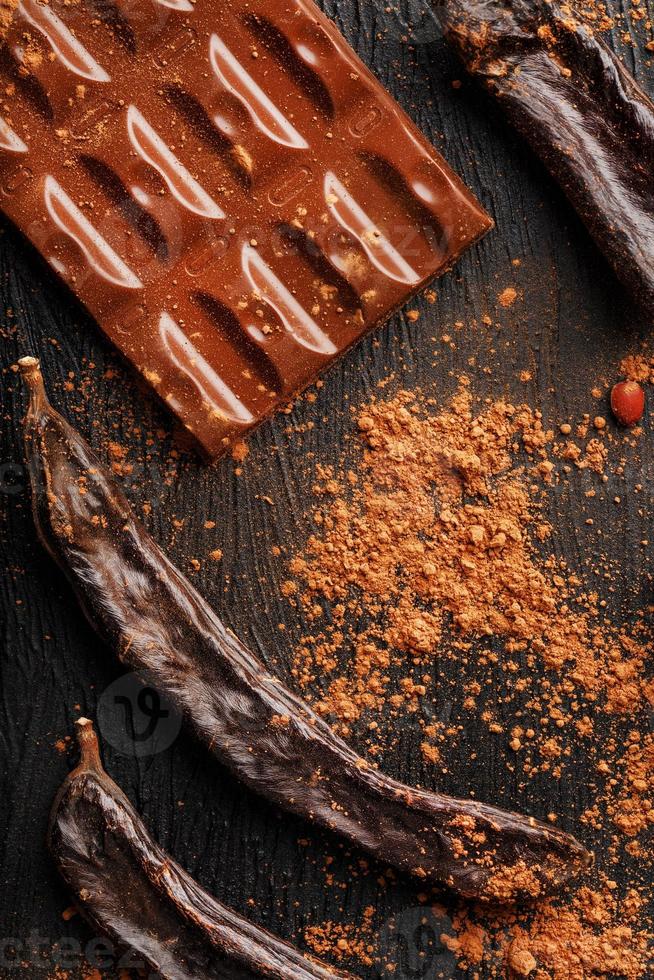 The pods of the carob chocolate bar on a black background. Sweets, chocolate and confectionery made of carob fruit. photo