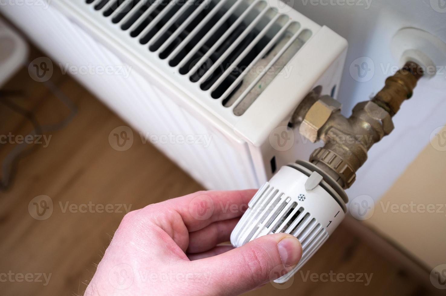 Hand turns the radiator thermostat to the minimum, due to rising gas prices. Concept of energy crisis and economy. photo