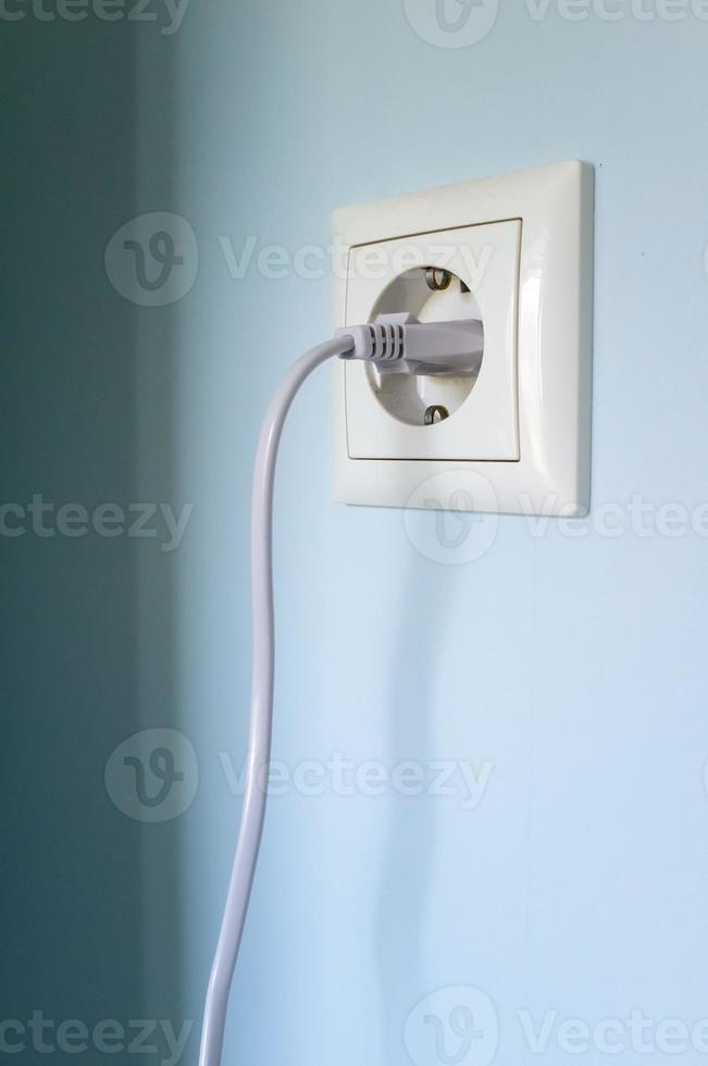 Plug with cable cord connected to the socket, on a blue wall. photo