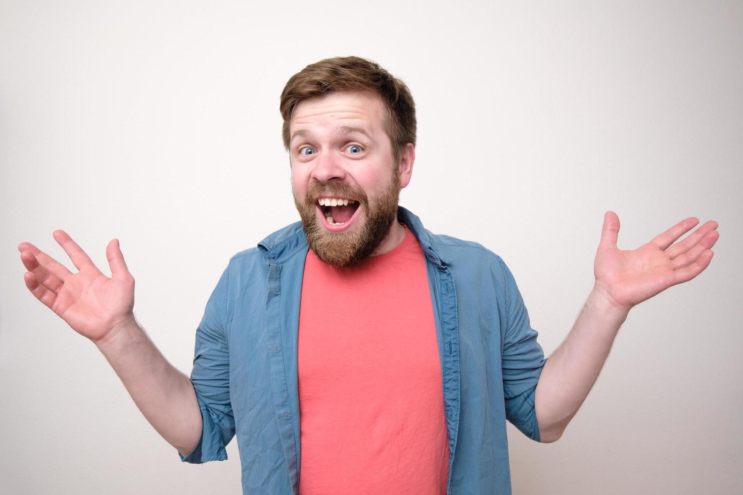 Charming, positive man makes a greeting gesture with arms outstretched to the side, he is smiling and looking at the camera happily. photo