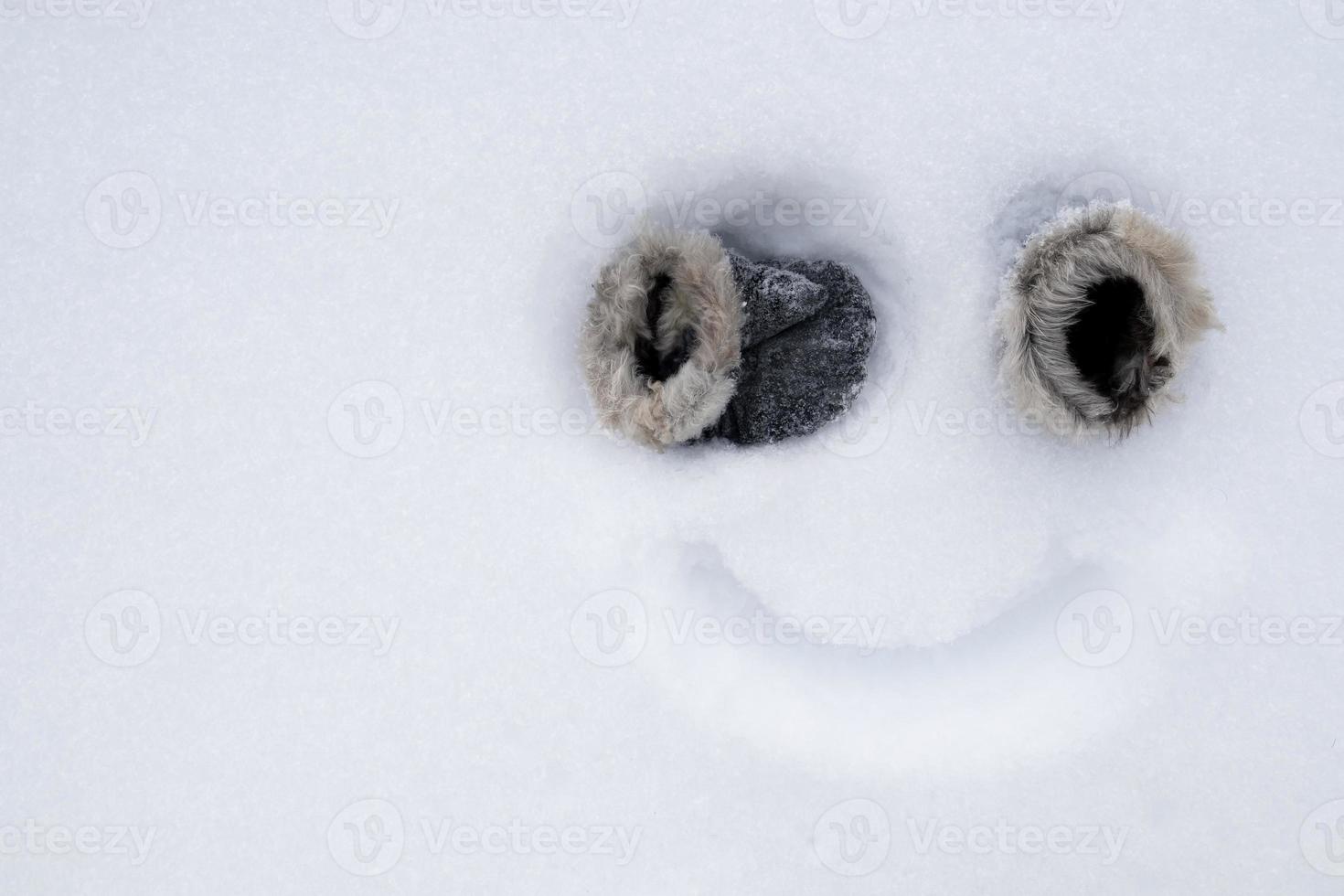 Funny homemade smiley face, with mittens instead of eyes and a painted smile on the snow. Creative idea. Copy space. Top view. photo