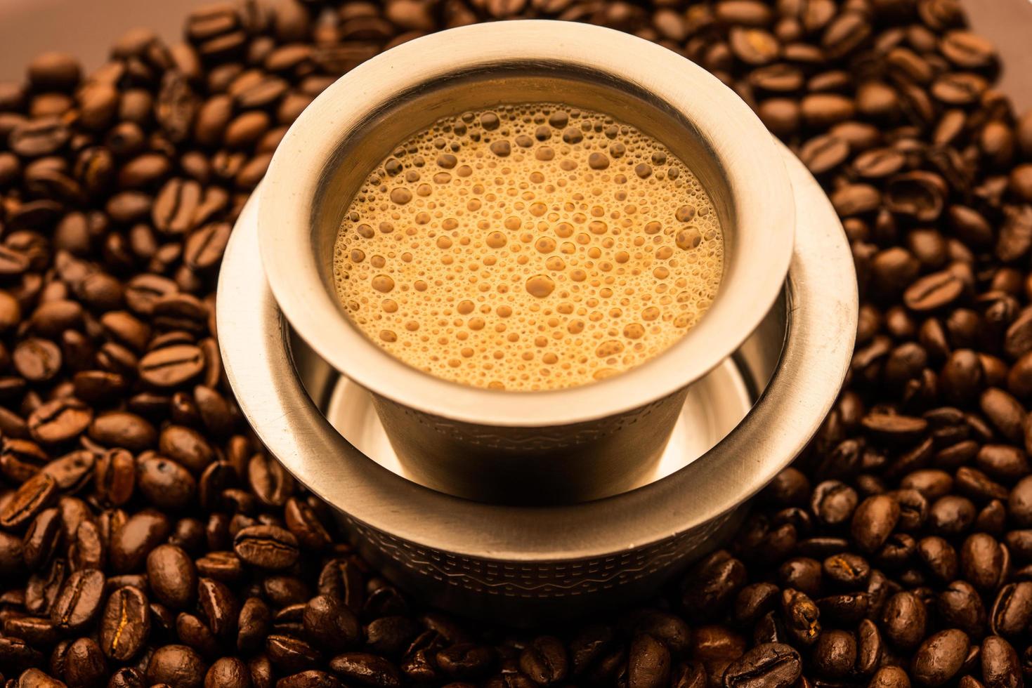 café de filtro del sur de la India servido en un vaso o taza tradicional sobre frijoles crudos tostados foto