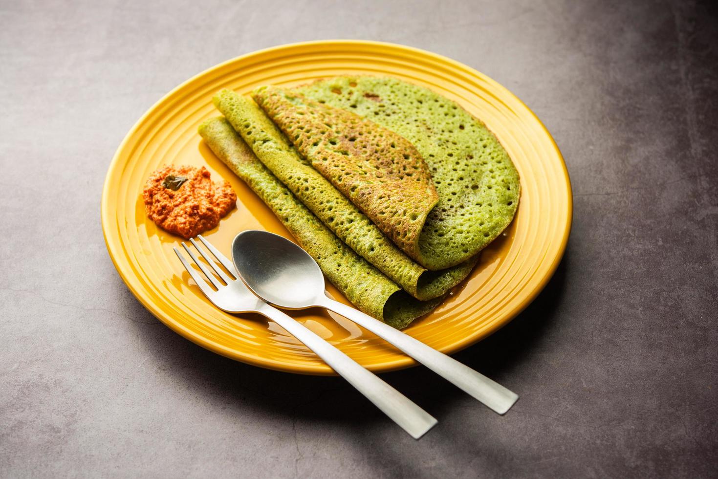 Palak dosa made using mixing spinach or keerai in batter, served with red chutney photo