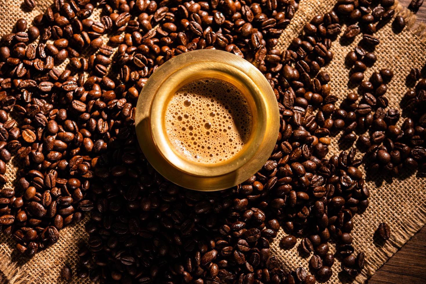 café de filtro del sur de la India servido en un vaso o taza tradicional sobre frijoles crudos tostados foto