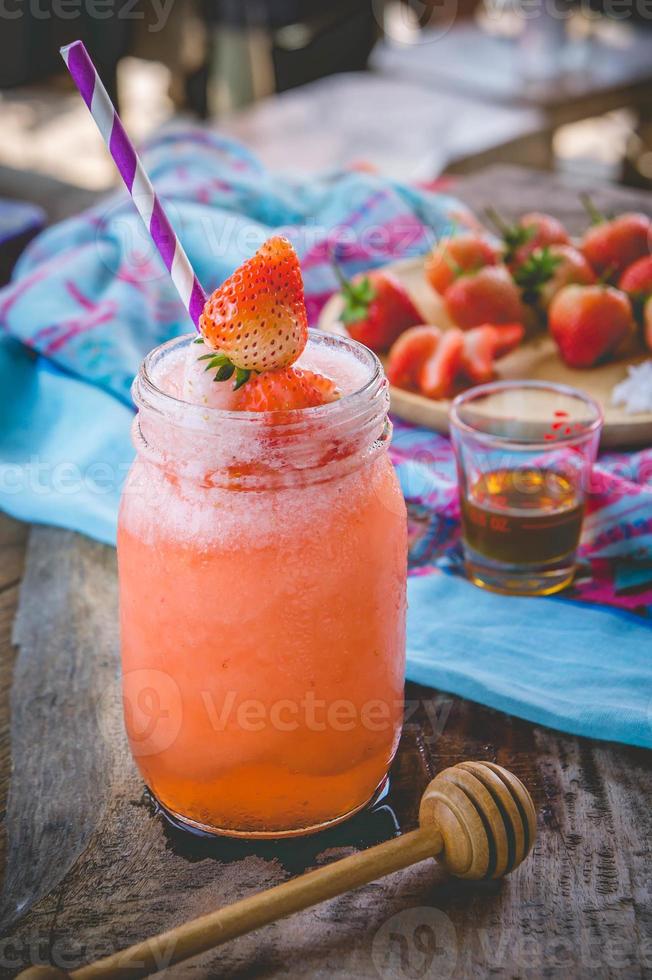 jugo de batido de fresa, sobre miel sabrosa para el verano en la mesa de madera, jugo de agua dulce para la salud foto