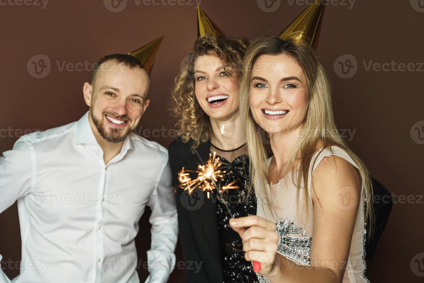 Happy people wearing party hats holding burning sparkles during holiday or event celebration photo