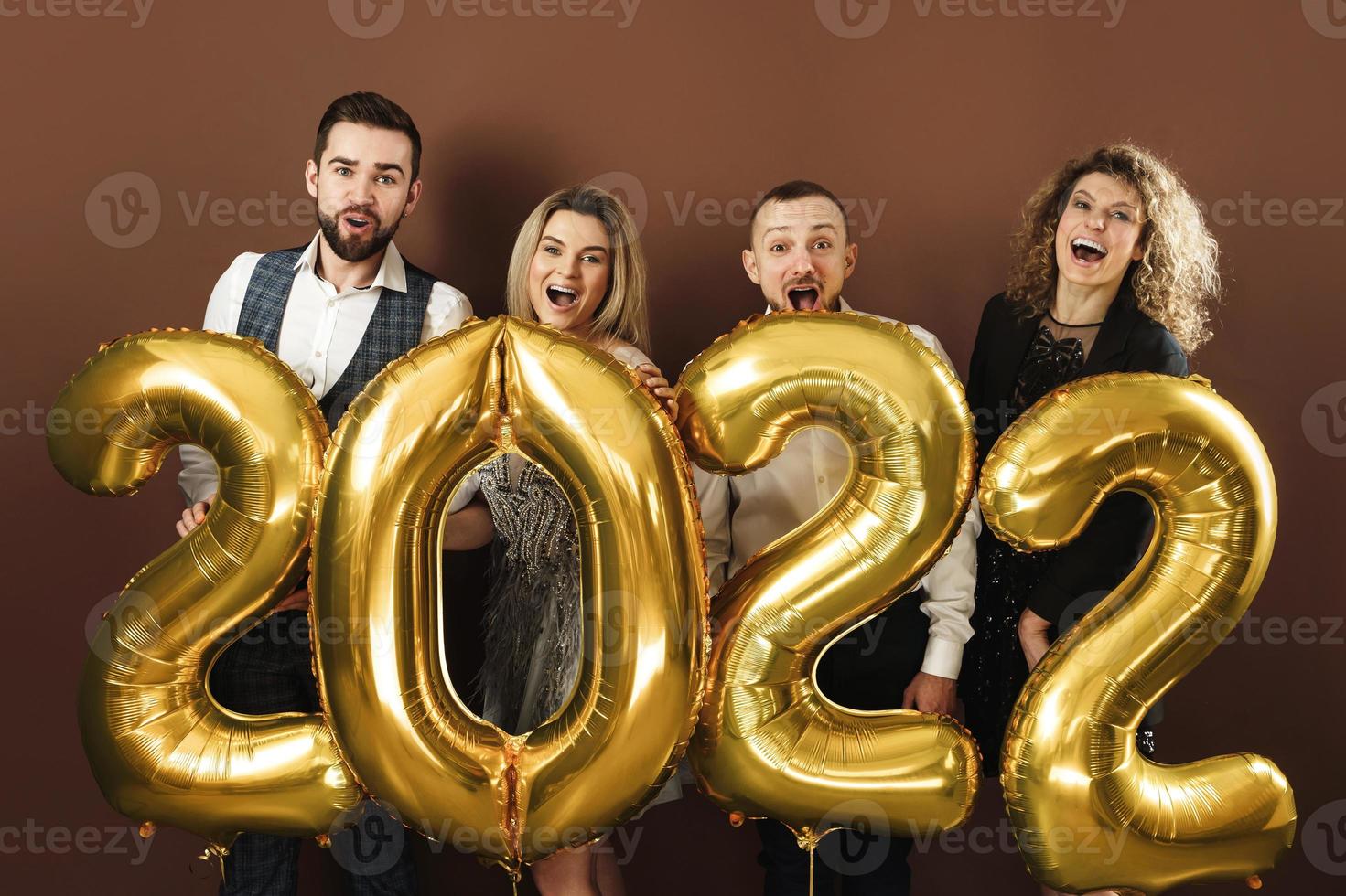 Group of beautiful well dressed party people celebrating arrival of 2022 New Year with a golden balloons photo