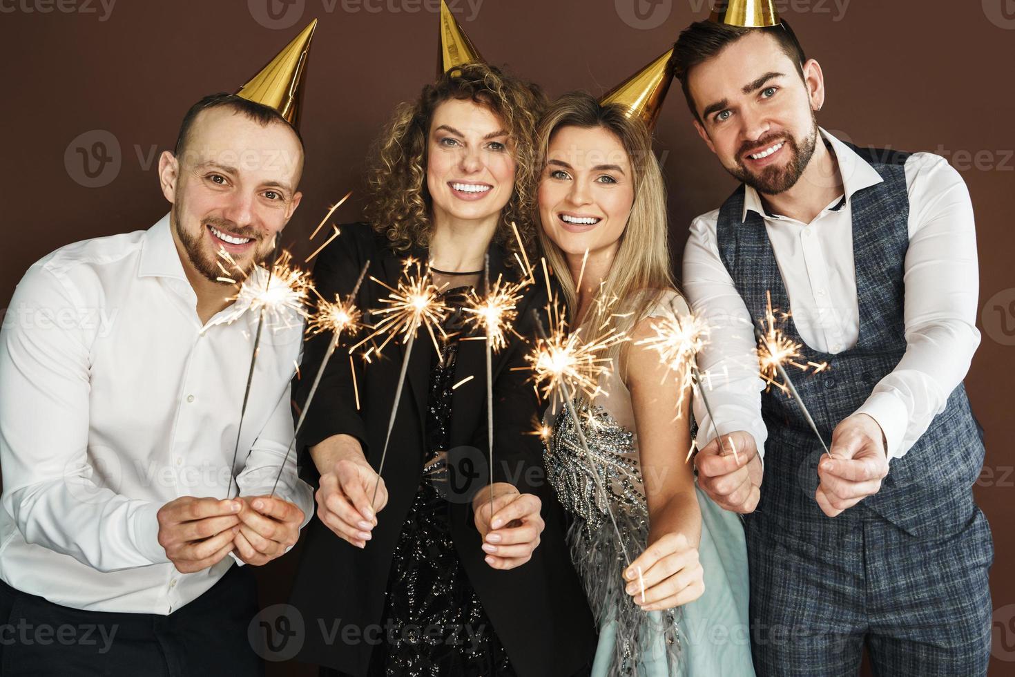 Happy people wearing party hats holding burning sparkles during holiday or event celebration photo