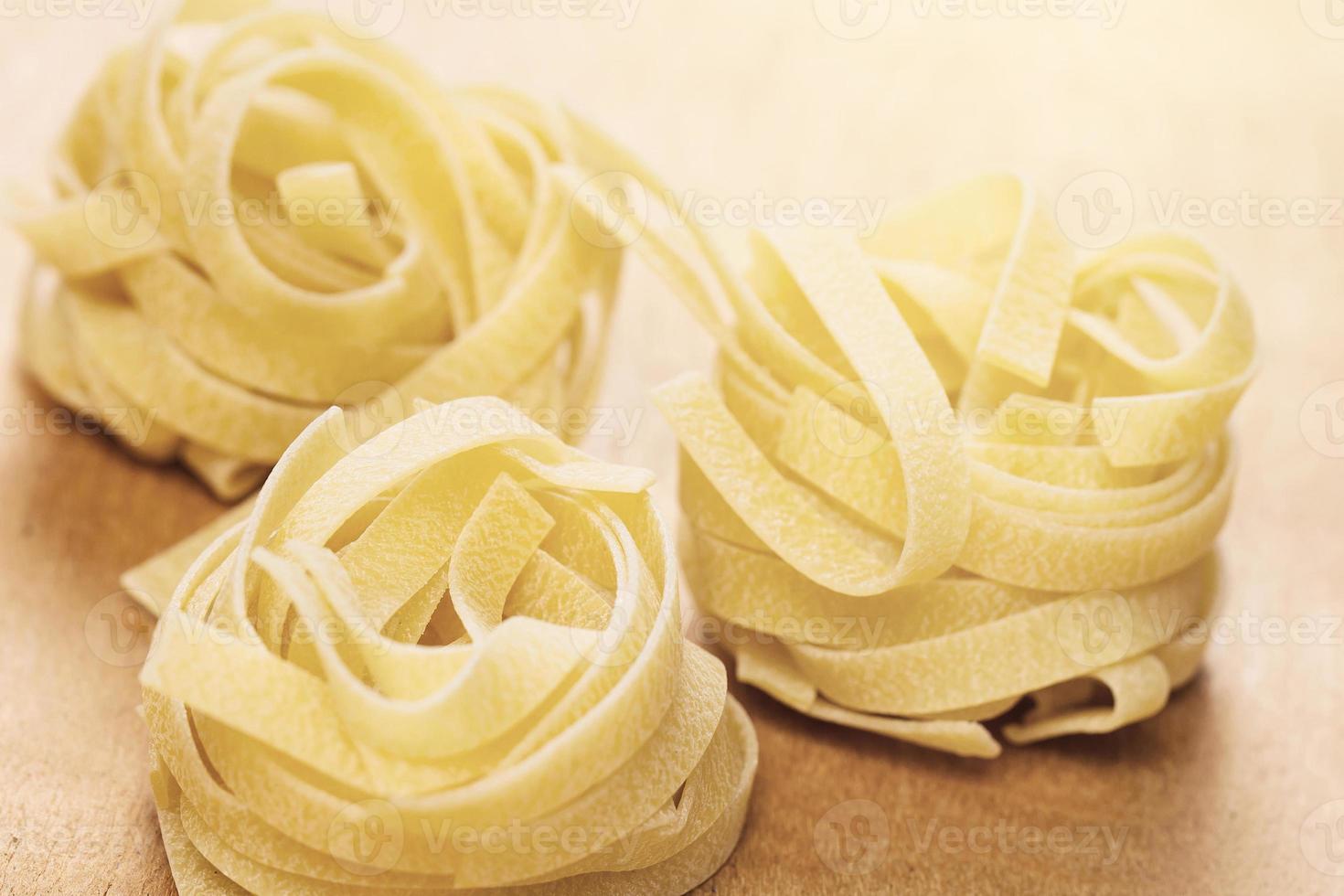 Uncooked tagliatelle pasta on wooden background photo