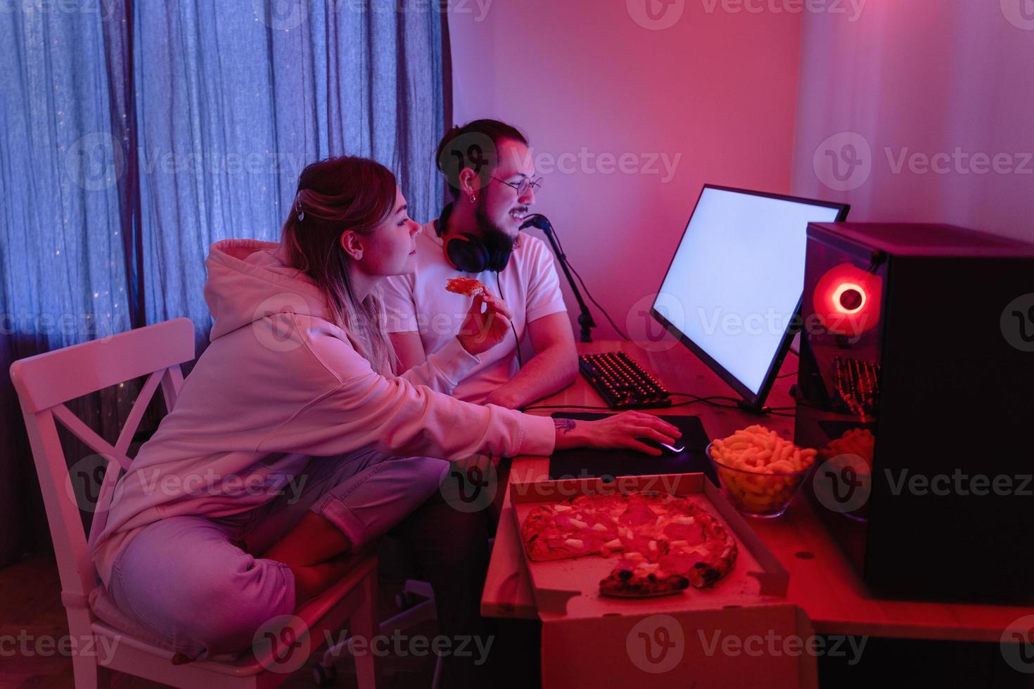 pareja relajándose en casa en una habitación con luz de neón y comiendo pizza, viendo películas en línea o jugando videojuegos foto