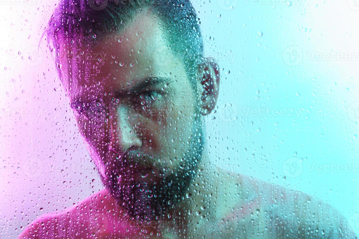 Portrait of handsome young man captured through wet glass in colorful light photo