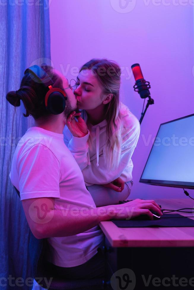 pareja joven besándose en la mesa con computadora personal de juego en luz de neón foto