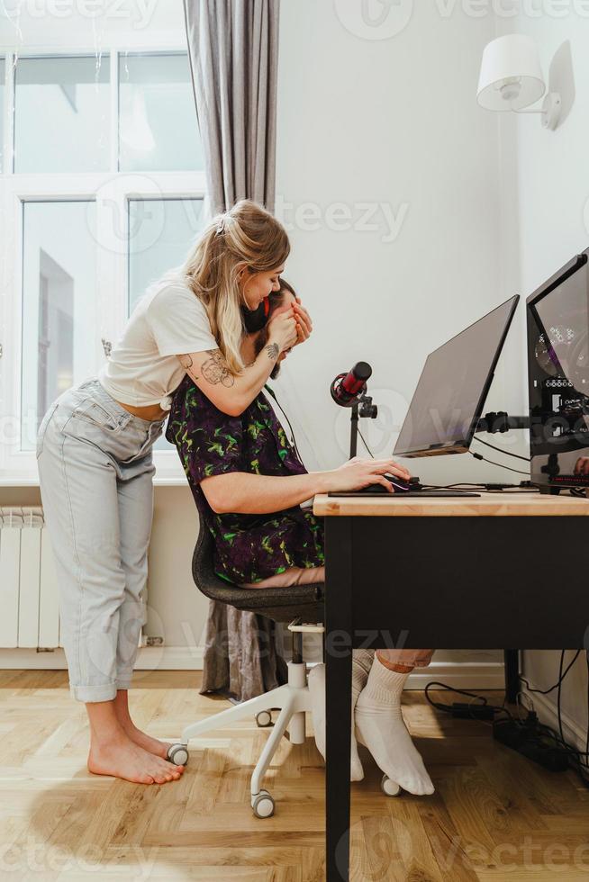 Girl covering her boyfriend's eyes and surprising him while he playing video game photo