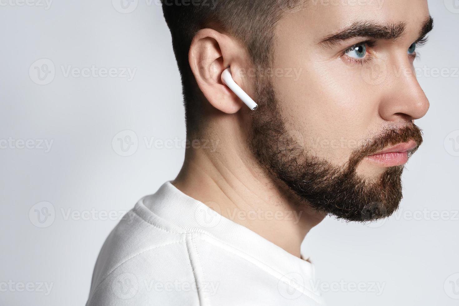 Handsome bearded man in white clothes using wireless earbuds photo