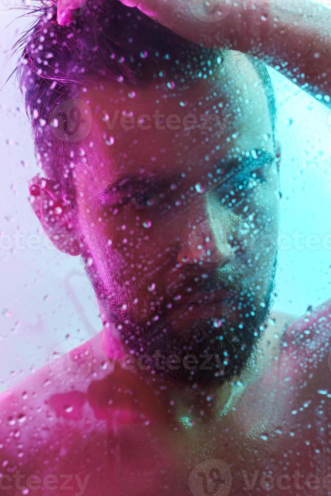 Portrait of handsome young man captured through wet glass in colorful light photo