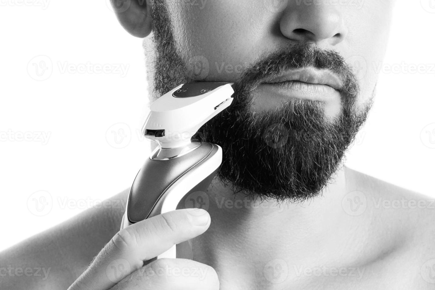 Handsome bearded man is using electric trimmer photo