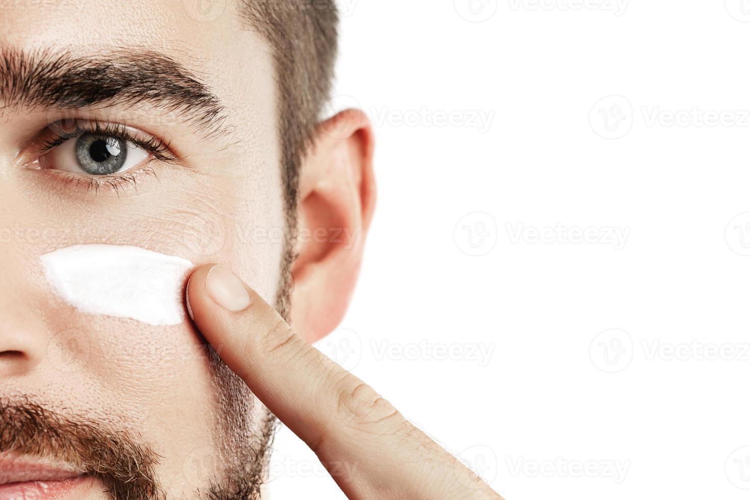 Young man is applying moisturizing and anti aging cream on his face photo