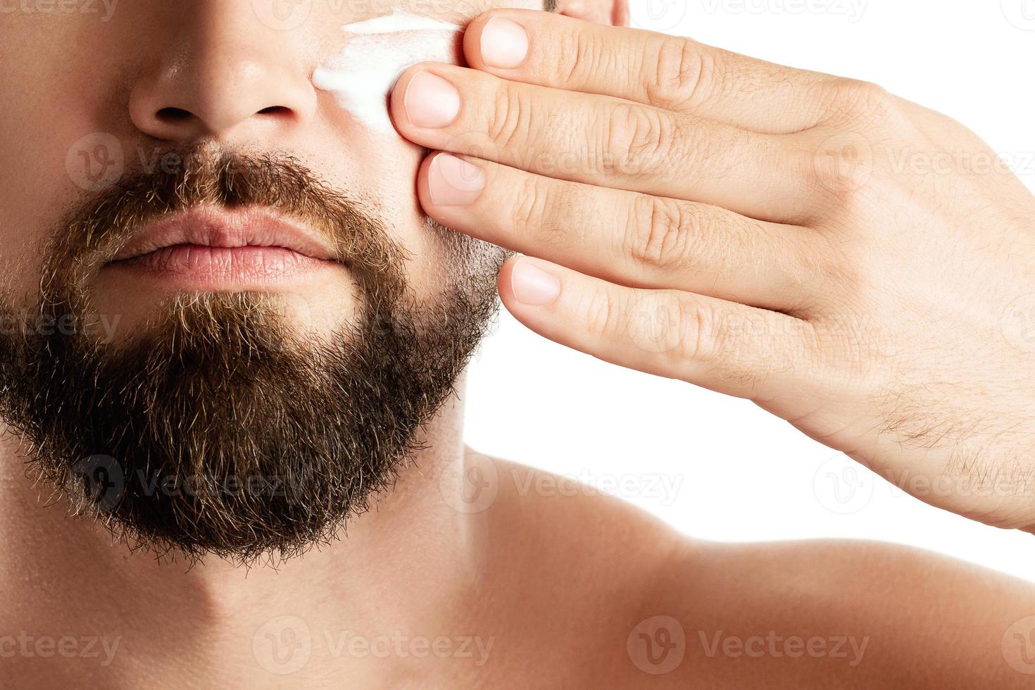 Young man is applying moisturizing and anti aging cream on his face photo