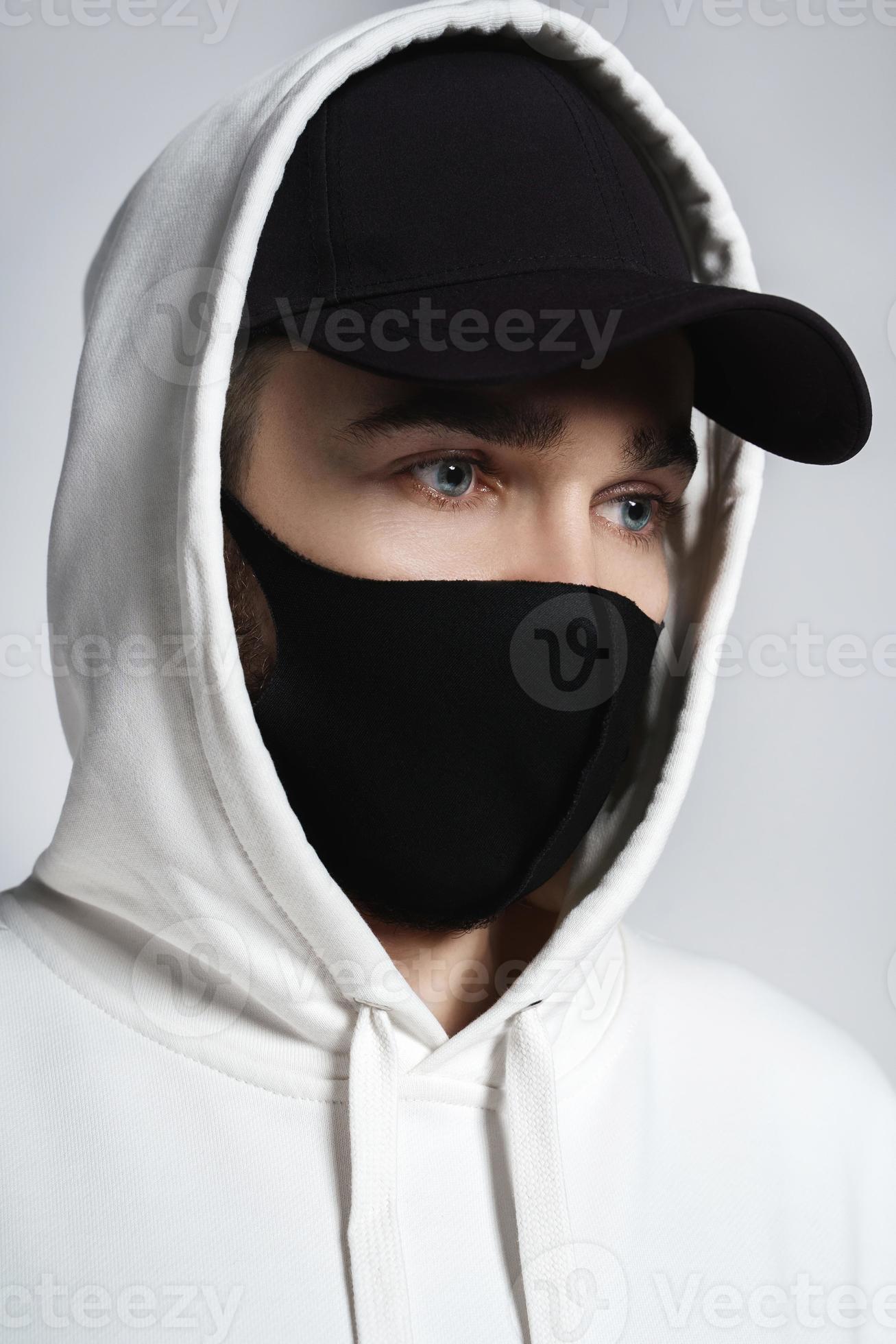 Man wearing white hoodie, black baseball cap and cloth face mask