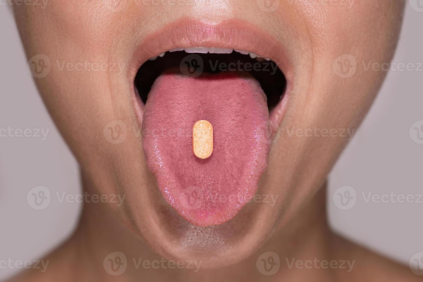 Half of female face with orange pill on tongue. photo