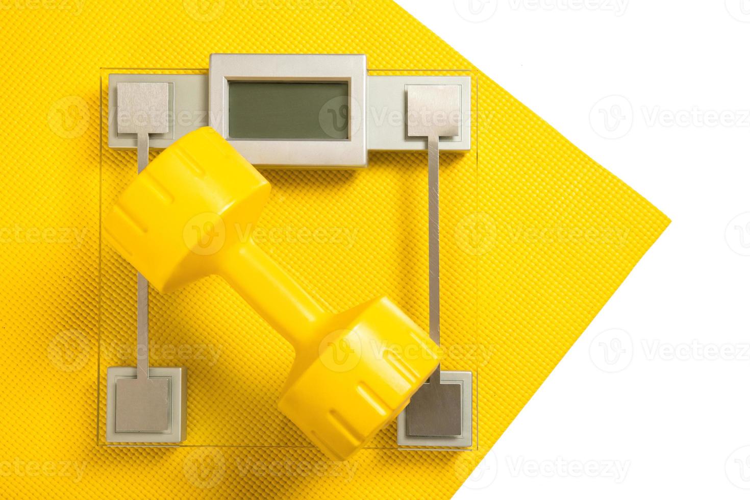 Yellow dumbbell and weight scale on fitness mat photo