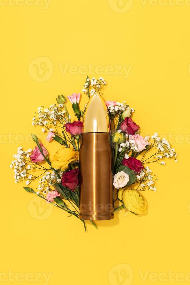 Pacifism and non-violence movement. Bullet and bunch of different flowers against yellow background. photo