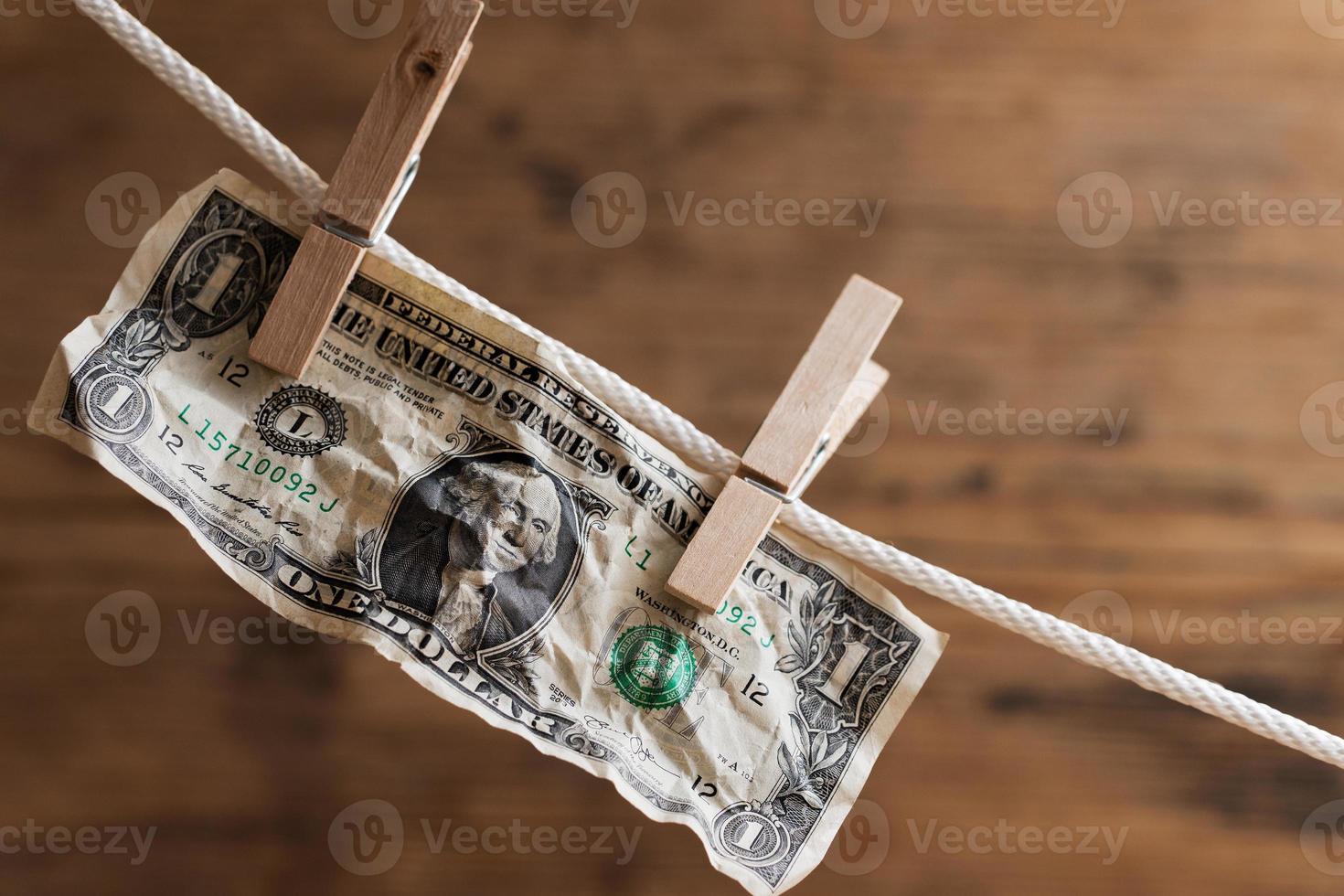 One dollar bill is drying on a white rope, held by laundry pins. photo