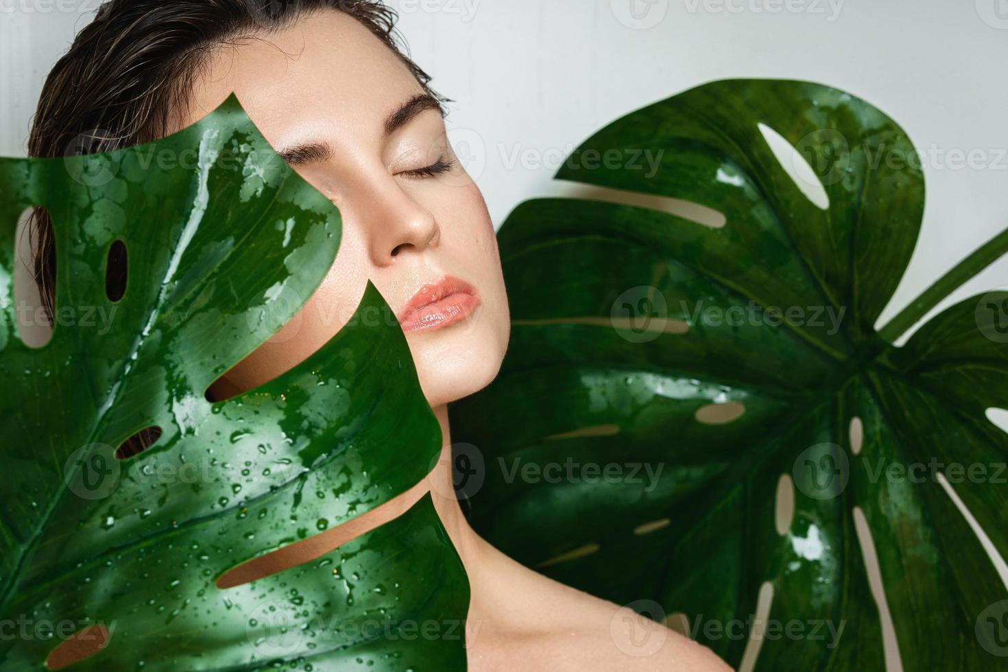 Young woman with a smooth skin holding Monstera deliciosa plant leaf photo