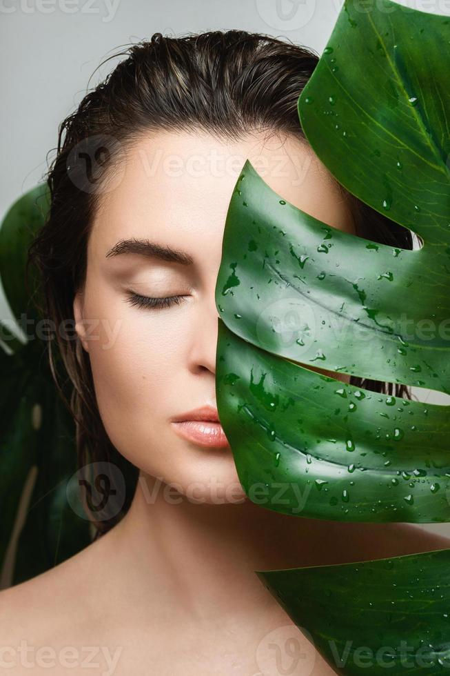 Young woman with a smooth skin holding Monstera deliciosa plant leaf photo