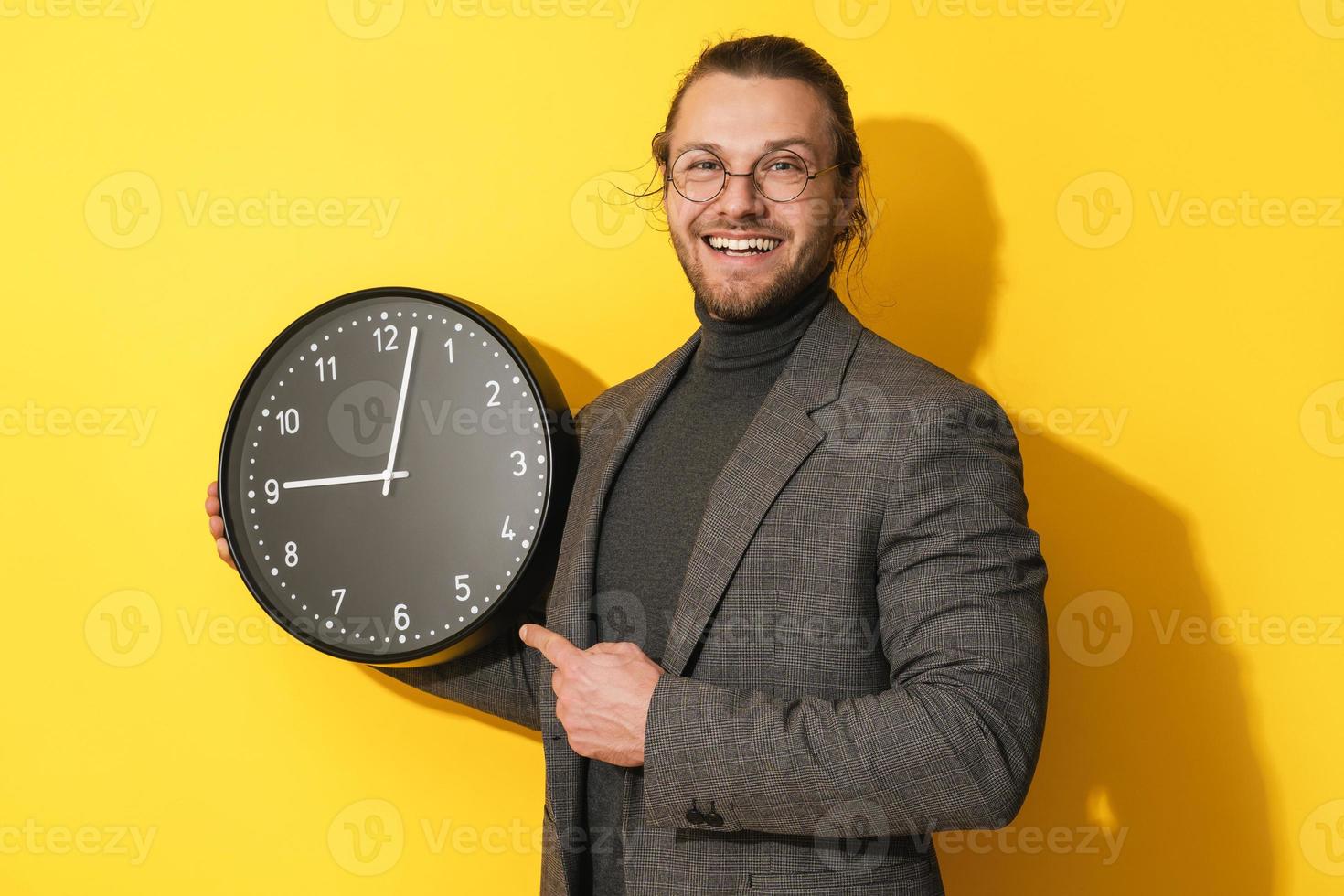 hombre alegre con gafas sosteniendo un gran reloj con fondo amarillo foto