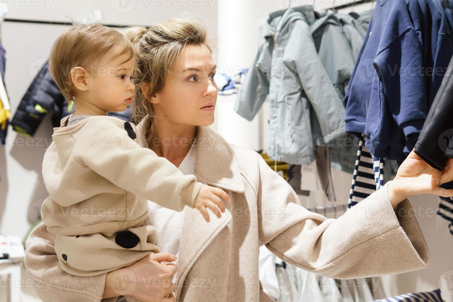 Woman with her baby son choosing clothing in clothes store photo