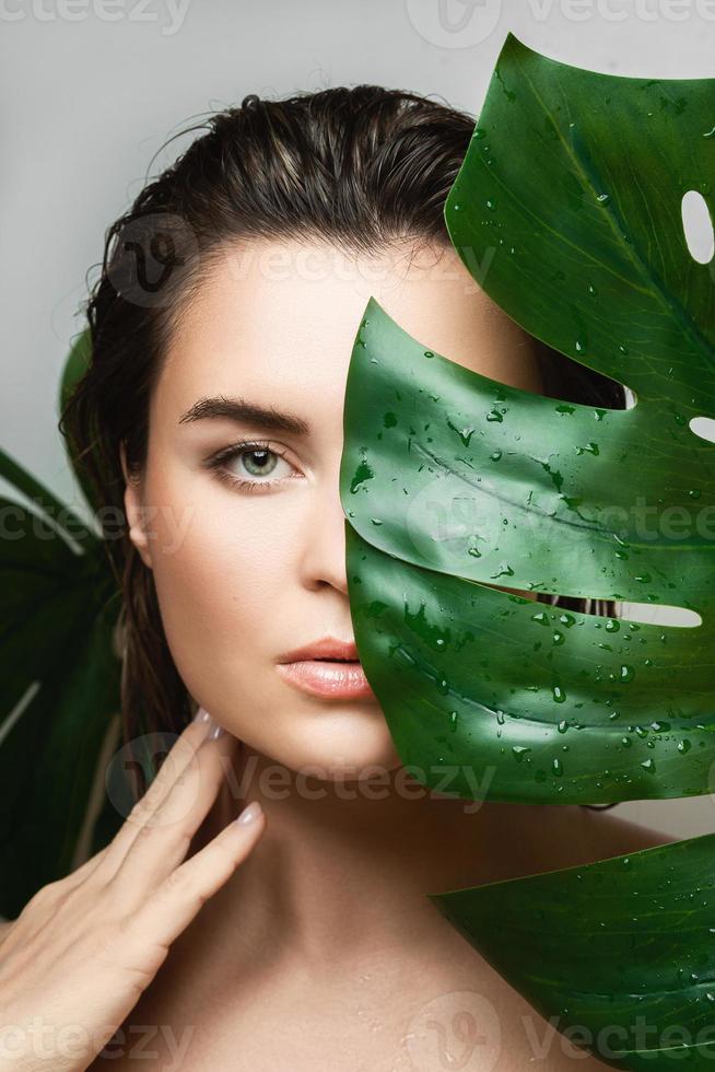 Young woman with a smooth skin holding Monstera deliciosa plant leaf photo