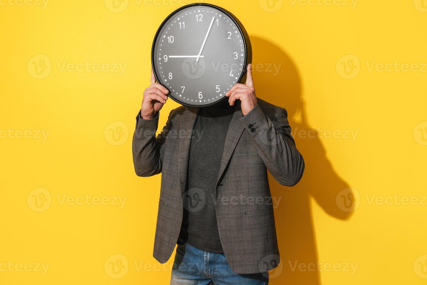 Man covering his face with  big clock on yellow background photo